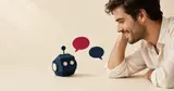 A man smiling at a small navy paper robot, two speech bubbles between them