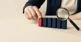A finger nudging a red block back into a row of navy blocks, a magnifying glass beside