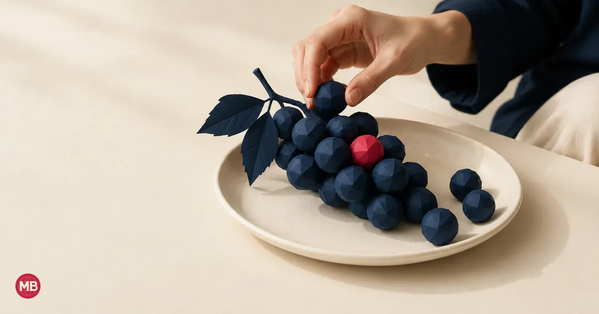Une main assemble des raisins en papier bleu marine en une grappe, un grain rouge